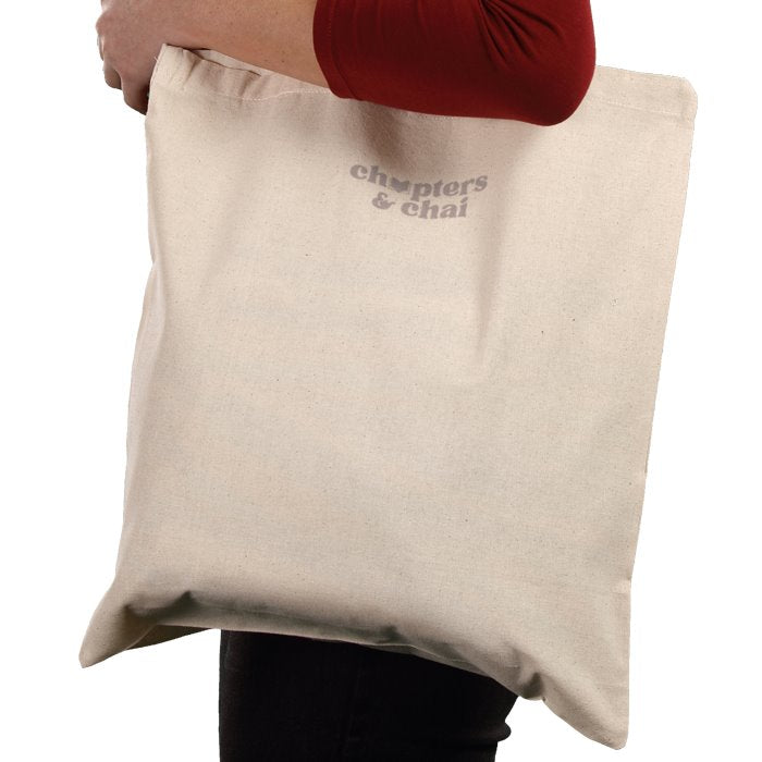 Beige tote bag held by a person with 'chapters & chai' branding.