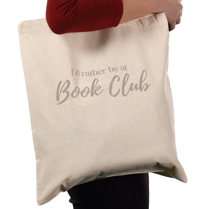 Beige tote bag with 'I'd rather be at Book Club' text held by a person.