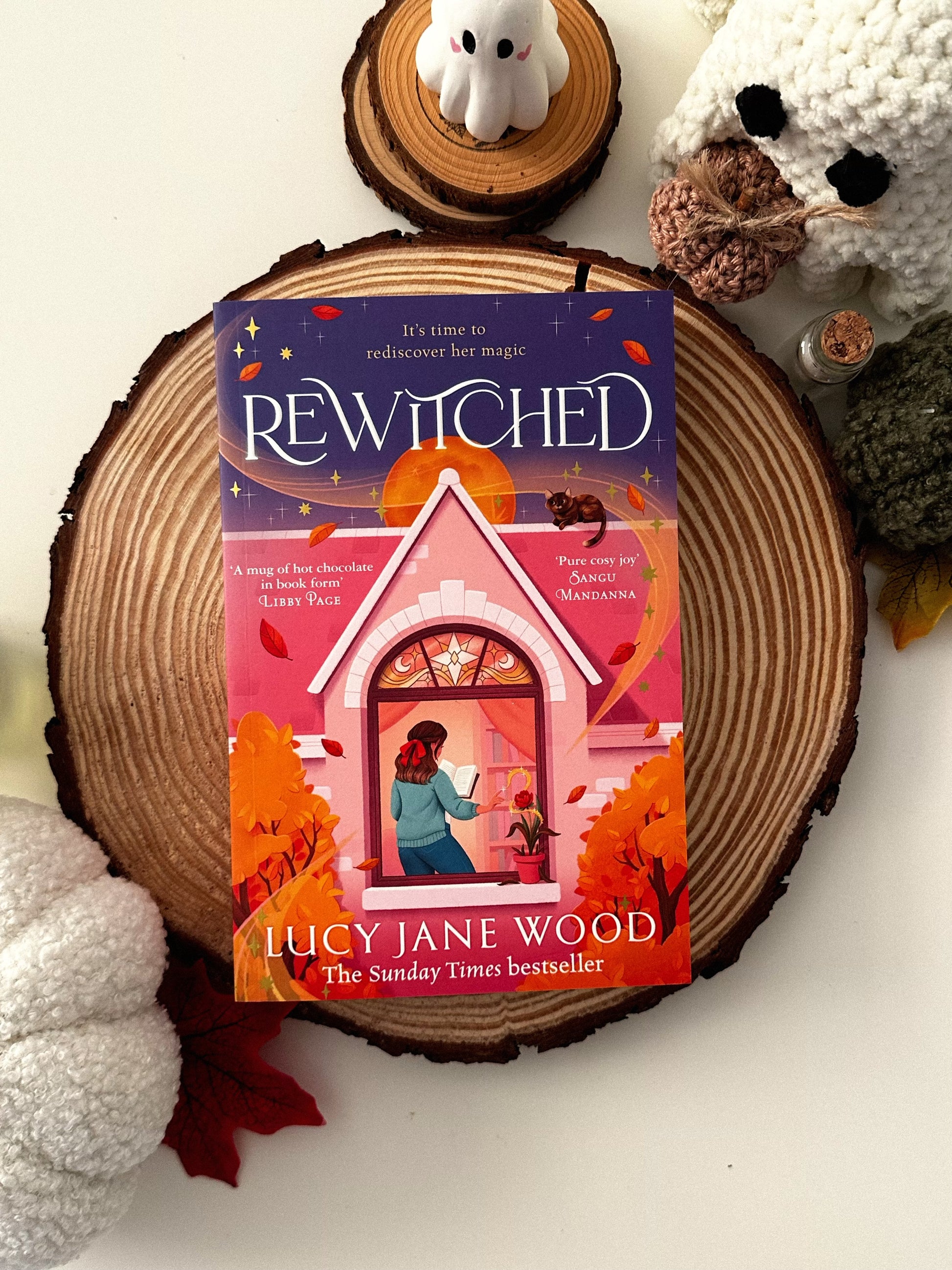 Book titled 'Rewitched' by Lucy Jane Wood on a wooden surface with decorative Halloween items.